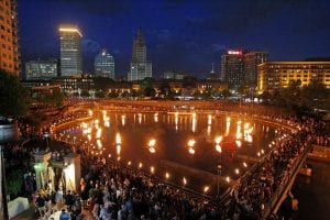 A view of the Providence River during the Waterfire celebration with basins lit up all over the river and people surrounding it.