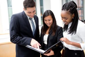 3 students looking onto a black folder and pointing at a document.