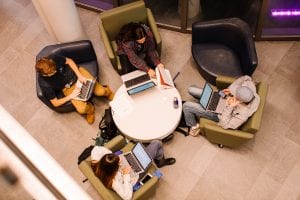 four students sitting down, studying, one with a laptop open, arial view