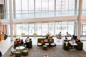 groups of students sitting sporadically in a bright atrium with windows to their backs, arial view 