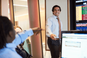 man in blue shirt and red tie looking at a student who is raising his hand, classroom setting