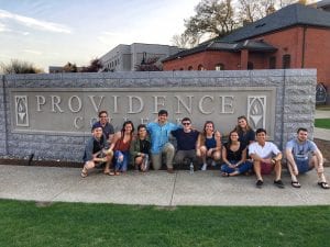 group of people dressed in summertime clothing huddled around Providence College sign in Huxley Circle