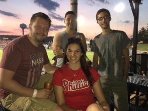 4 interns in a group, one with a red Phillies shirt on, posing in a baseball stadium