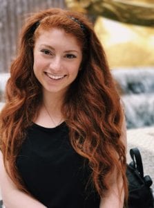 headshot of a woman smiling at the camera, long red hair, outside