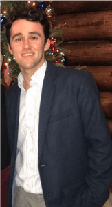 white male with brown hair, a white shirt, and a blue jacket posing directly in front of the camera