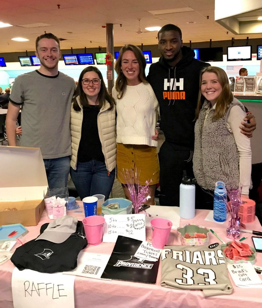 Five students stand behind a raffle table at a bowling fundraiser.