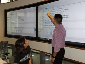 Professor pointing at formulas on a digital white board.