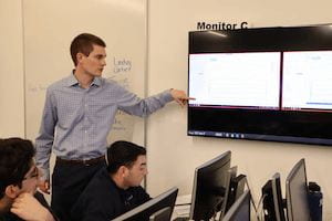 Professor Jon Jackson pointing at a chart on a digital screen while students at computers look on.