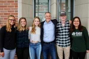 6 people posed in front of a wall with a window looking at the camera