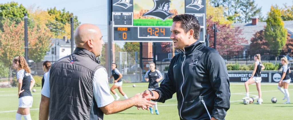 Two soccer coaches shake hands on a soccer field