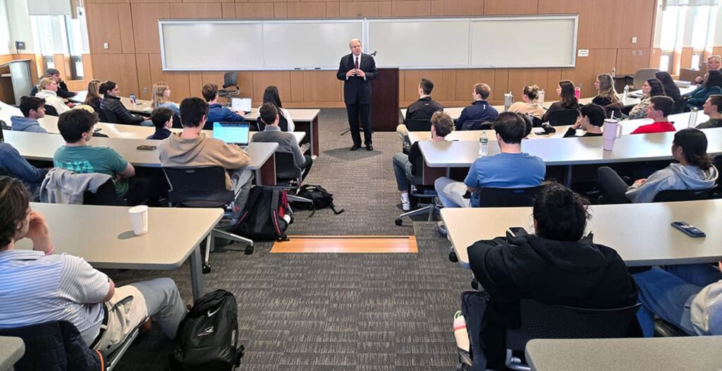Gene Dodaro standing center speaking to an audience of the students