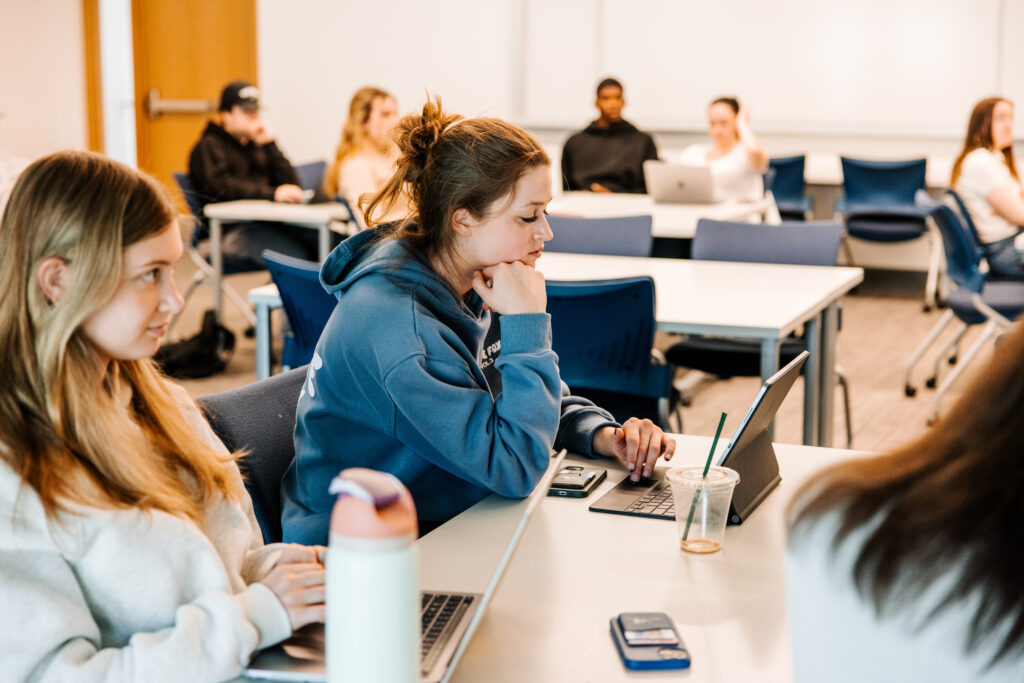 Two students at a table looking at their laptops