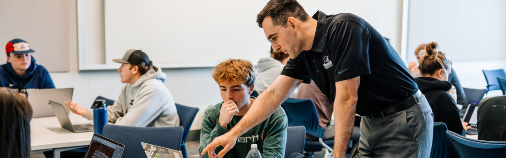 Management professor pointing at a laptop with a student seated