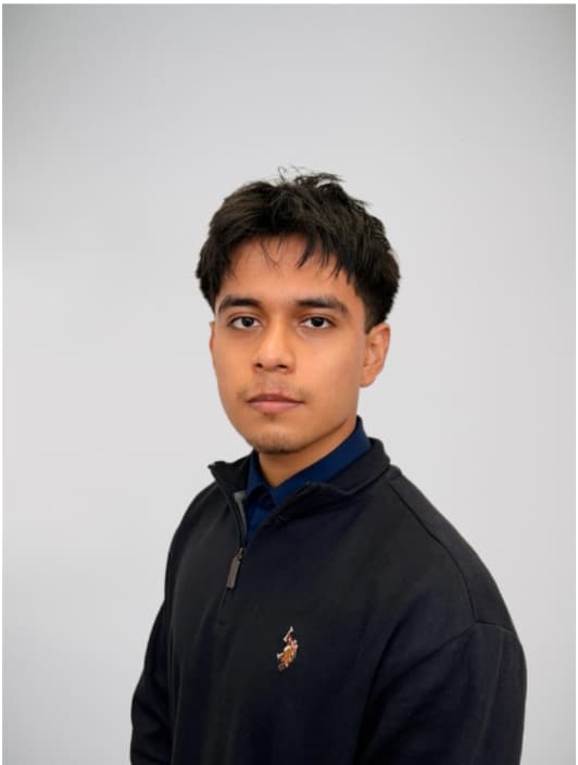 A young man with brown hair and brown eyes in a black quarter zip standing against a gray background.