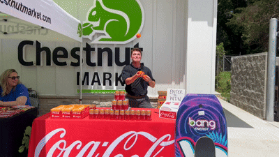 Mikey Stamatis juggling behind a table with cans of coke on it. He is wearing a black Coca-Cola polo